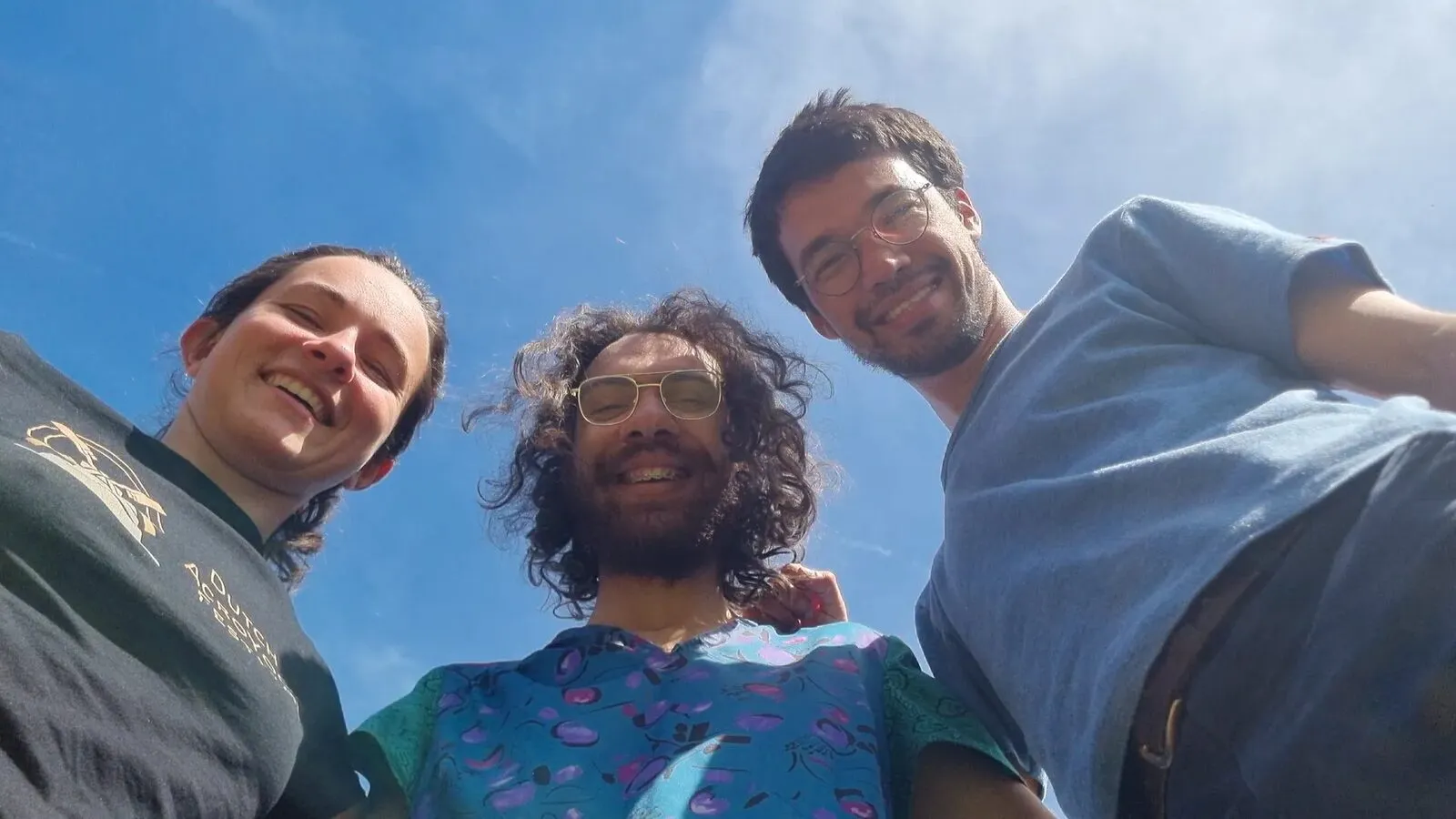 Trois ami·es souriants contre un ciel bleu clair, vue contre-plongée