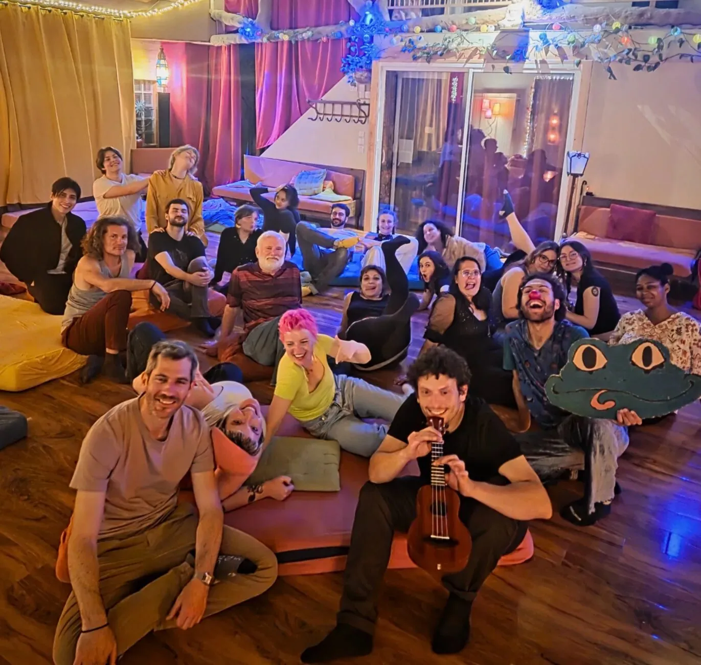 Groupe de personnes assises au sol dans une ambiance chaleureuse, sourires et coussins